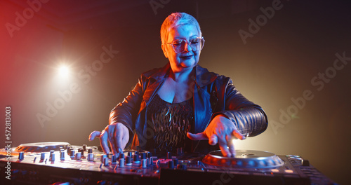 Fotografia A cool caucasian dj grandma is composing a mix at turntables controller