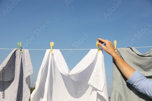 Woman hanging clothes with clothespins on washing line for drying against blue sky outdoors, closeup