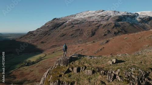 Hiker on rocky outcrop admiring view with reveal of snowy mountains and hiker exit at Wasdale Lake District UK photo