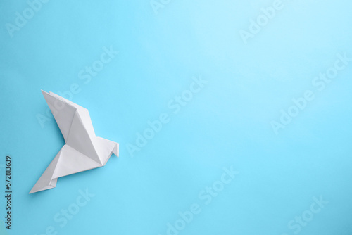 Origami art. Beautiful handmade paper bird on light blue background, top view. Space for text