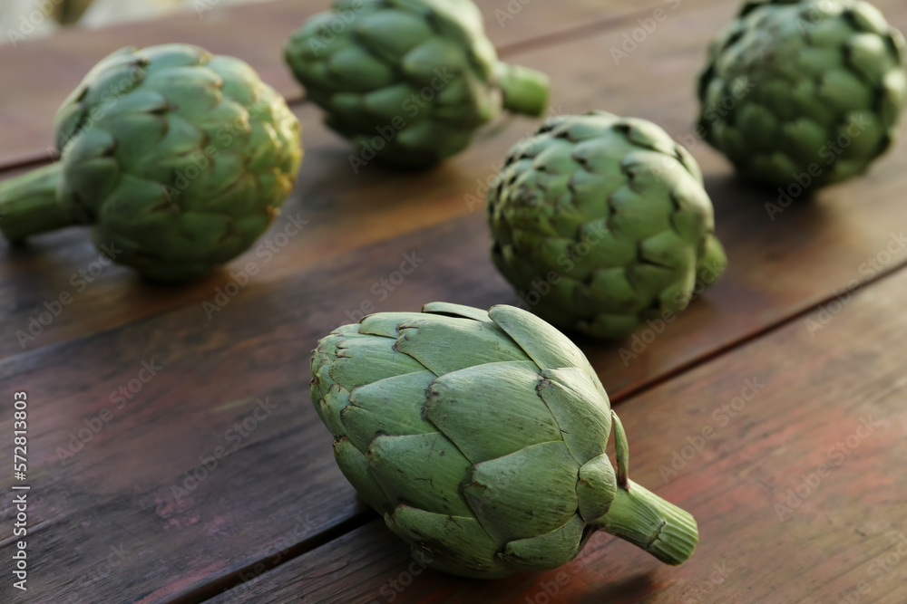 Fototapeta premium Whole fresh raw artichokes on wooden table, closeup