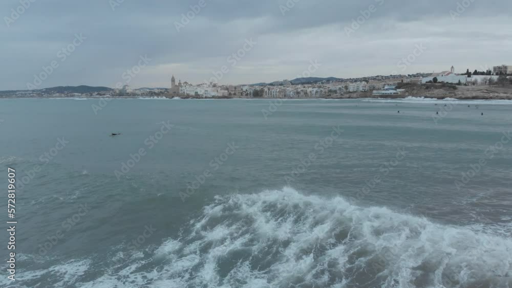 drone captures crashing waves against rocks and then flies over surfers waiting for next wave near coastal town drone captures crashing waves against rocks and then flies over surfers waiting for next wave near coastal town