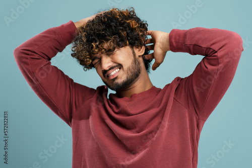 Young Indian man scratching his head on blue background. Pediculosis concept. Man with lice and nits