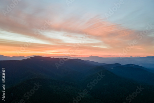Aerial view of dark mountain hills with bright sunrays of setting sun at sunset. Hazy peaks and misty valleys in evening © bilanol