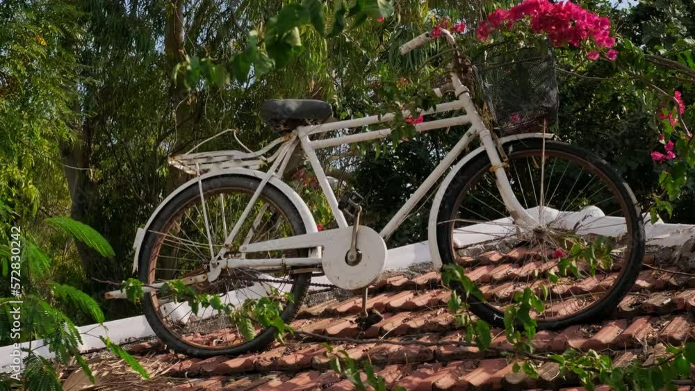 old retro bicycle is installed on roof of small building as monument. White vintage bicycle statue in flowers. old retro bicycle is installed on roof of small building as monument. White vintage bicycle statue in flowers.