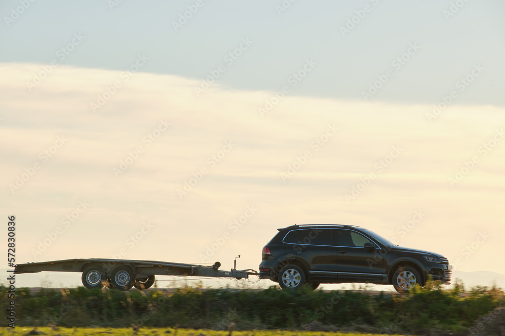 Tow truck vehicle with car transporting carrier trailer driving on highway in evening