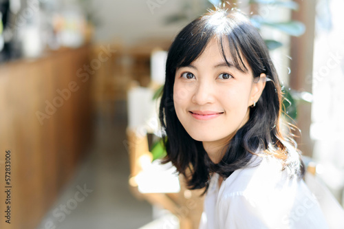 Brightly smiling beautiful young asian woman sitting in coffee cafe in sunny day