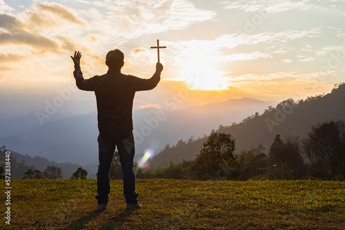Male Travel holding christian cross praying alone on top mountain sunset background Lifestyle spiritual relaxation emotional concept vacations outdoor harmony with nature landscape © AungMyo