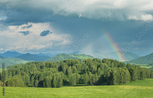 Stormy sky with a rainbow in the countryside  green meadows  mountains and hills