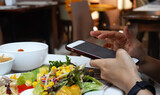  Man hand using or looking at his smartphone and having lunch in the restaurant with friends