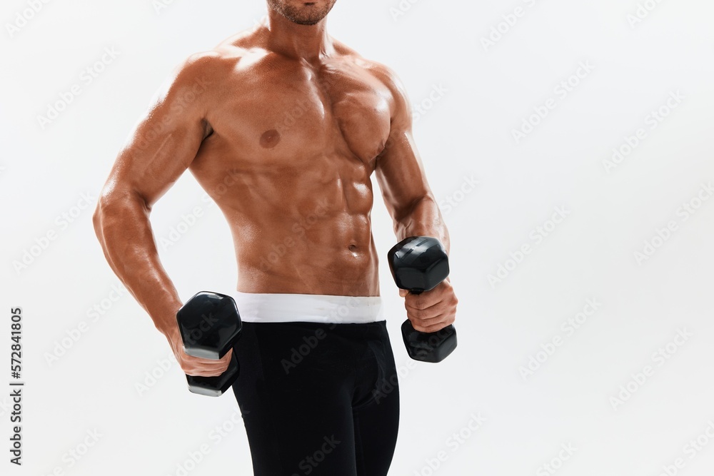 Fototapeta premium Man athletic body bodybuilder posing with dumbbells with naked torso abs full-length in the background, fitness class. Advertising, sports, active lifestyle, competition, challenge concept.