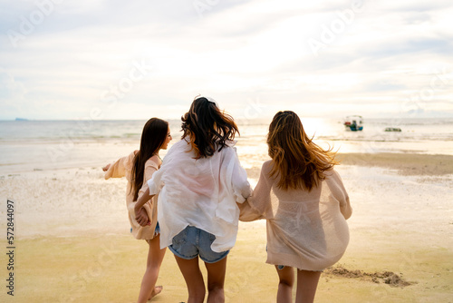 Canvas Print Group of Young Asian woman friends in walking and playing sea water together on tropical island beach at summer sunset