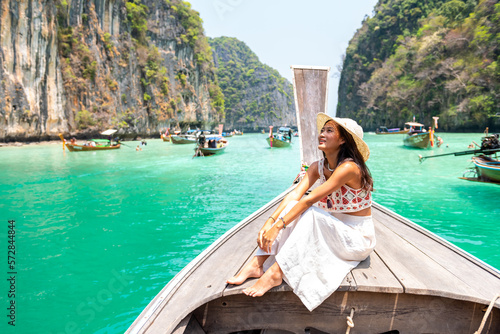 Happy Asian woman sitting on ship bow and looking beautiful nature of tropical island lagoon in Thailand. Attractive girl relax and enjoy outdoor lifestyle travel on boat on summer beach vacation.