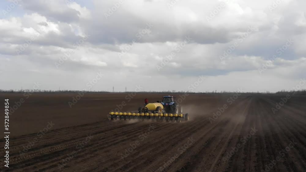 Blue tractror planting sunflower with yellow planter on the cultivated field in Ukraine Blue tractror planting sunflower with yellow planter on the cultivated field in Ukraine