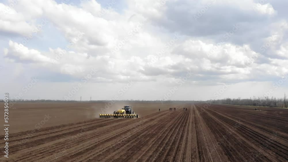 Blue tractror planting sunflower with yellow planter on the cultivated field in Ukraine Blue tractror planting sunflower with yellow planter on the cultivated field in Ukraine