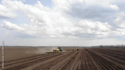 Blue tractror planting sunflower with yellow planter on the cultivated field in Ukraine photo