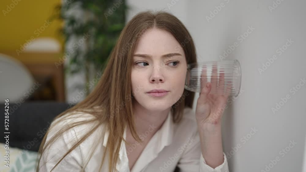 Young blonde woman spying neighbours with glass on wall at street Young blonde woman spying neighbours with glass on wall at street