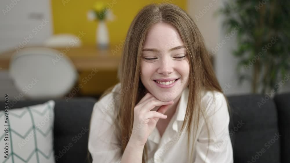 Young blonde woman smiling confident sitting on sofa at home