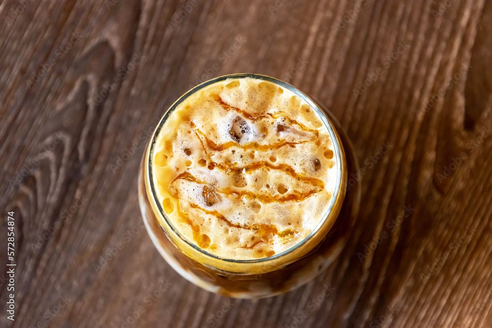Glass of iced caramel macchiato on wooden table on background. Glass of iced caramel macchiato on wooden table on background.