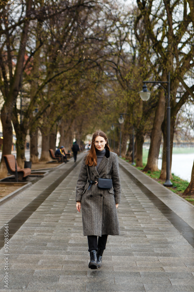 woman in a woolen coat walks alone in the middle of a spring city