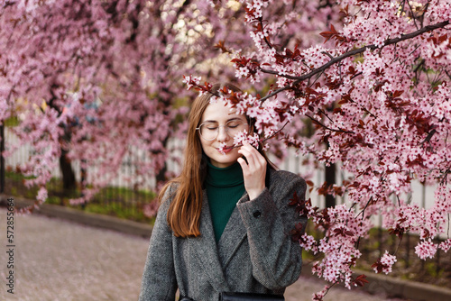 young woman in a woolen coat walks among cherry blossoms in spring