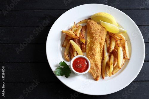 Pesce e patatine britanniche tradizionali in piatto bianco su sfondo di legno.