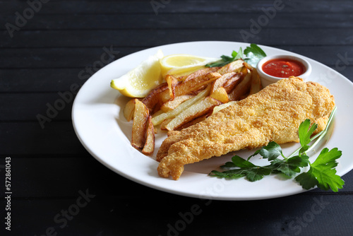 Pesce e patatine britanniche tradizionali in piatto bianco su fondo di legno.