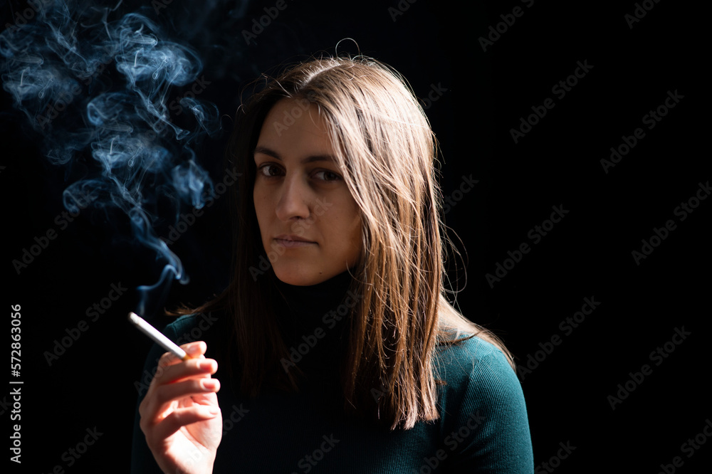 Fototapeta premium Young woman smoking cigarette on black background