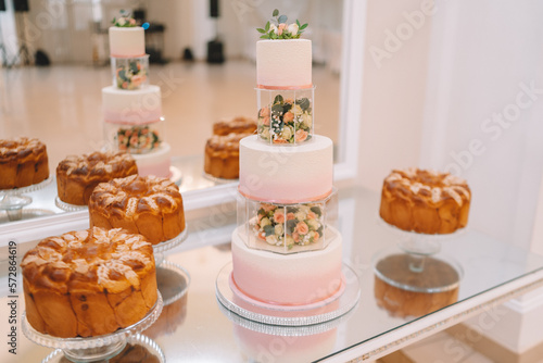 White wedding cake decorated by flowers standing on festive table with lots of snacks on side. Violet flowers on foreground. Wedding. Recetion photo