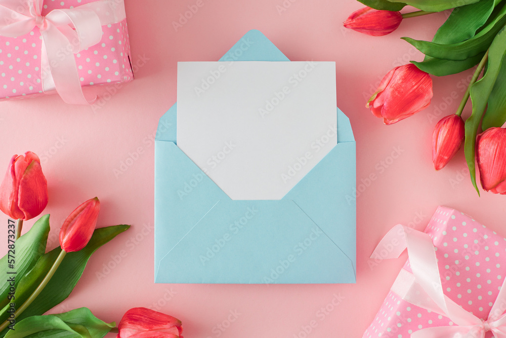Woman day concept. Top view photo of gift boxes with tulips flowers on pastel pink background and envelope with white card in the middle. Greeting card idea.