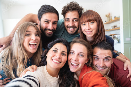 A group of friends taking a selfie at home. They are all gathered together, with big smiles on their faces .