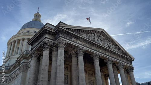 Pantheon building in Paris, France with focus on French flag over blue sky.