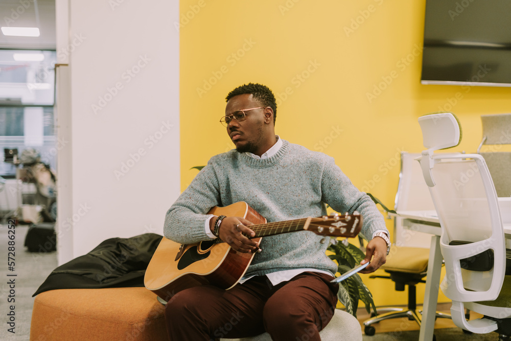 Good looking black male person preparing to play a guitar for his colleagues