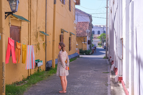 Young woman standing on a narrow street in the old town in front of  hanging and drying bright clothes on a rope © Tatonka