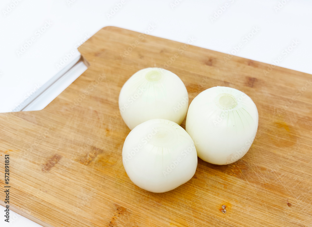 Peeled whole fresh onion on wooden cutting board, isolated on white background. Peeled whole fresh onion on wooden cutting board, isolated on white background.