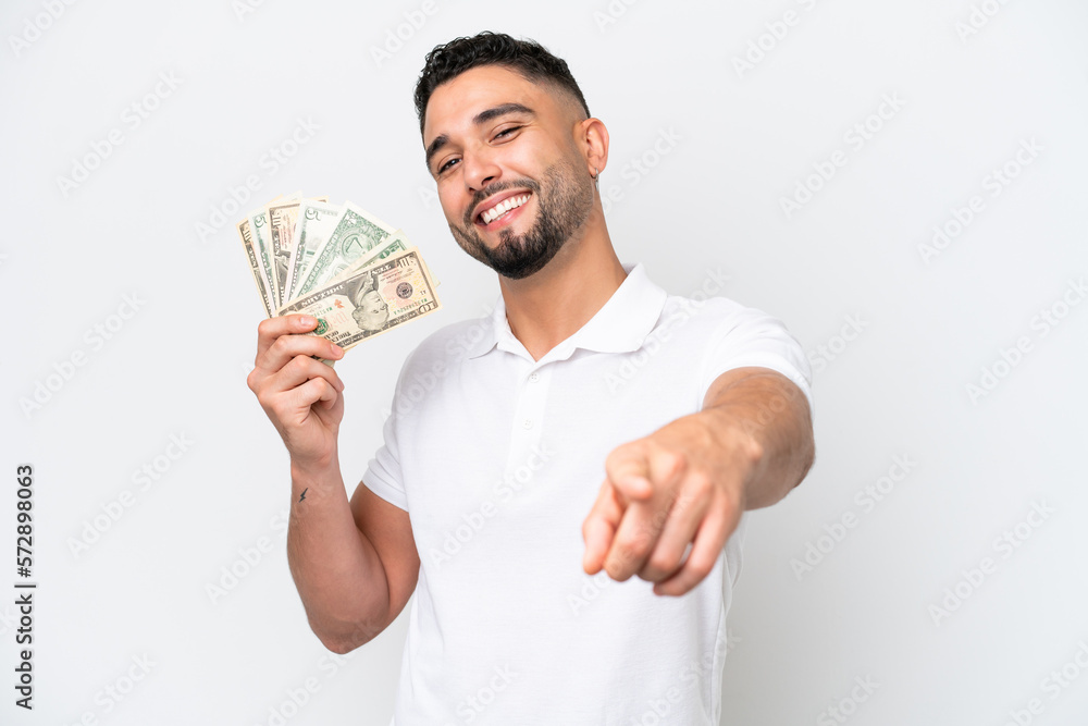 Young Arab man taking a lot of money isolated on white background pointing front with happy expression Young Arab man taking a lot of money isolated on white background pointing front with happy expression