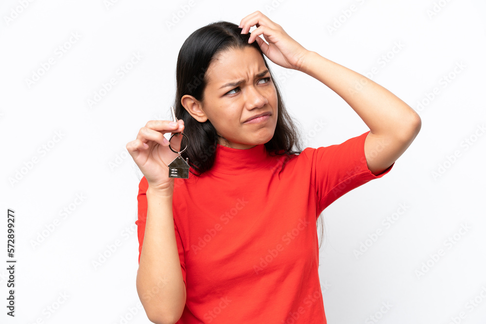 Young Colombian woman holding home keys isolated on white background having doubts and with confuse face expression Young Colombian woman holding home keys isolated on white background having doubts and with confuse face expression
