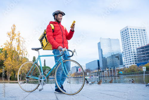 Food delivery rider man at street checking the client address on phone app. Pizza courier backpack