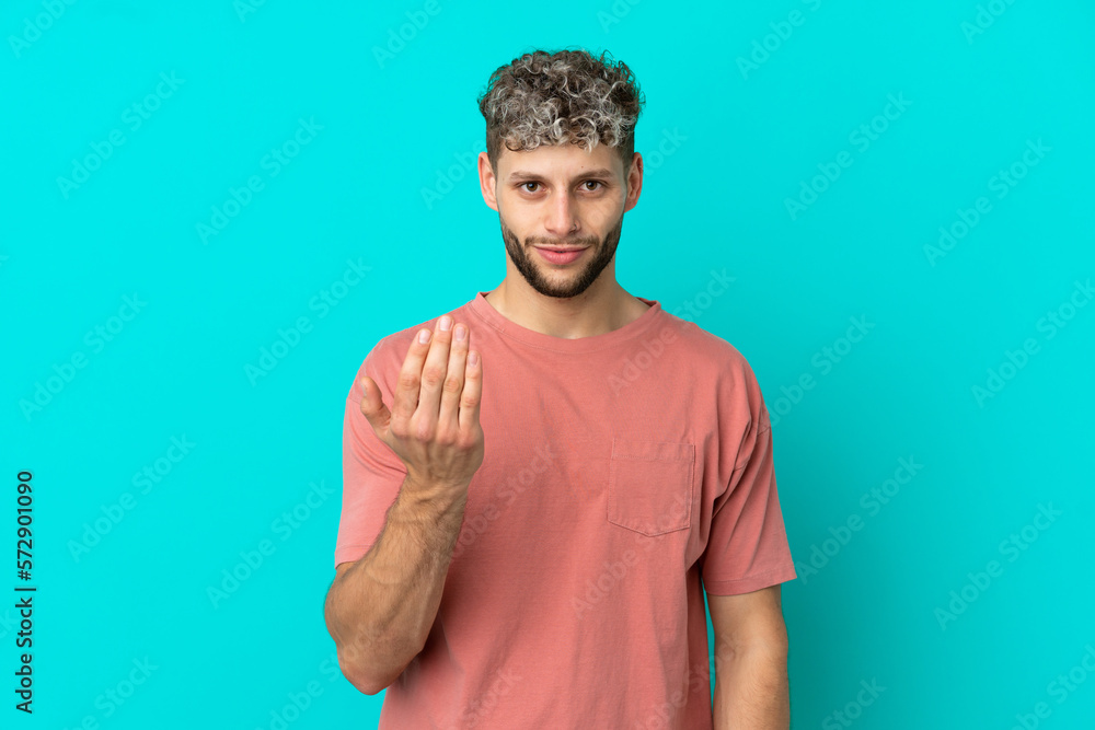 Young handsome caucasian man isolated on blue background inviting to come with hand. Happy that you came Young handsome caucasian man isolated on blue background inviting to come with hand. Happy that you came