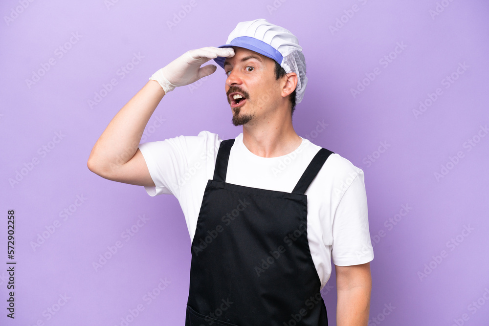 Fishmonger man wearing an apron isolated on purple background doing surprise gesture while looking to the side Fishmonger man wearing an apron isolated on purple background doing surprise gesture while looking to the side