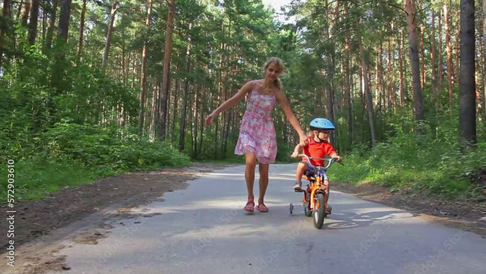 Young mother, helping her son to learn how to ride a bike, holding him and teaching him Young mother, helping her son to learn how to ride a bike, holding him and teaching him