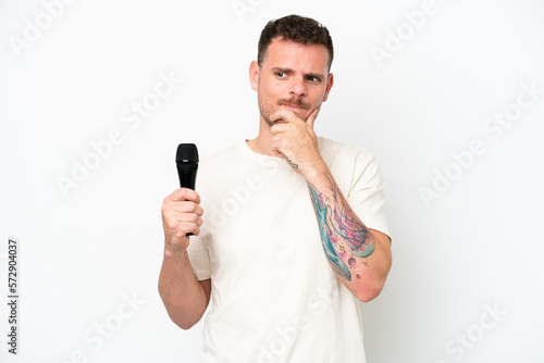Young caucasian singer man picking up a microphone isolated on white background having doubts and thinking