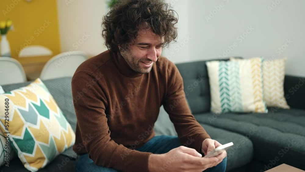 Young hispanic man using smartphone sitting on sofa at home Young hispanic man using smartphone sitting on sofa at home