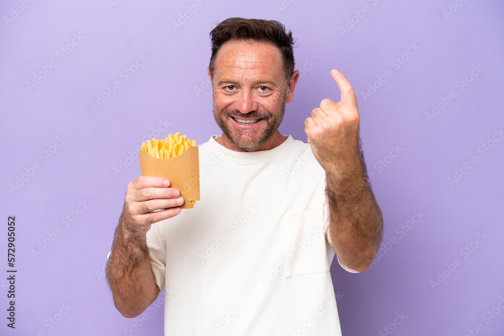 Middle age caucasian man holding fried chips isolated on purple bakcground doing coming gesture Middle age caucasian man holding fried chips isolated on purple bakcground doing coming gesture