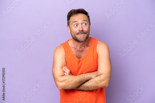 Middle age caucasian man isolated on purple background making doubts gesture while lifting the shoulders