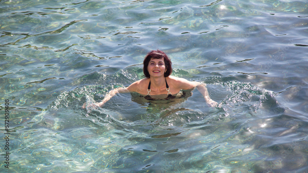Beautiful woman black swimsuit bathes in the sea.