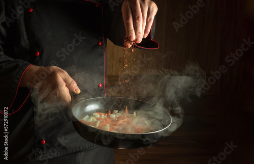 Fototapeta Naklejka Na Ścianę i Meble -  Experienced chef adds spices to fried carrots with onions in a frying pan. Cooking vegetables for lunch. Place for restaurant menu or recipe