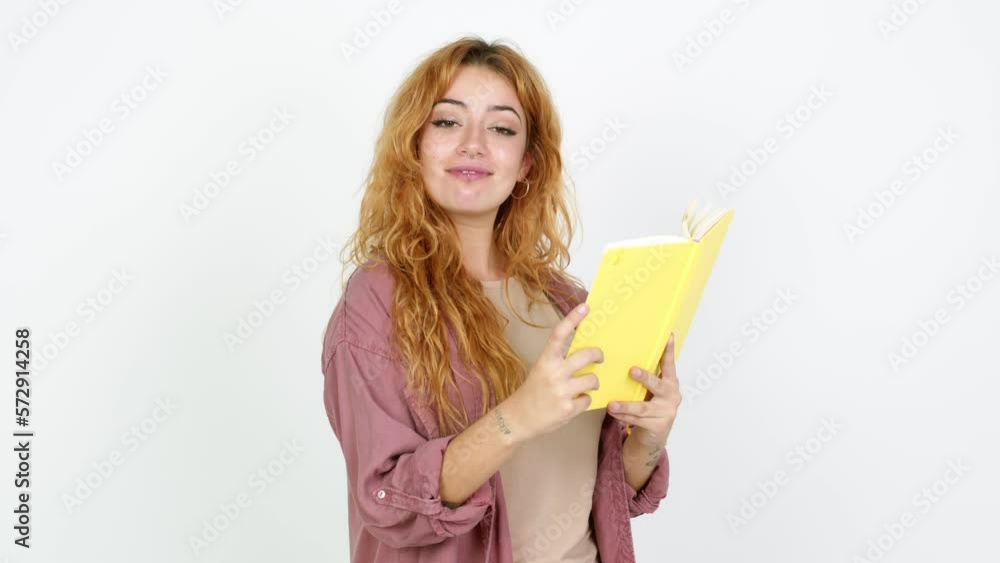 Young redhead woman holding a book over isolated background Young redhead woman holding a book over isolated background