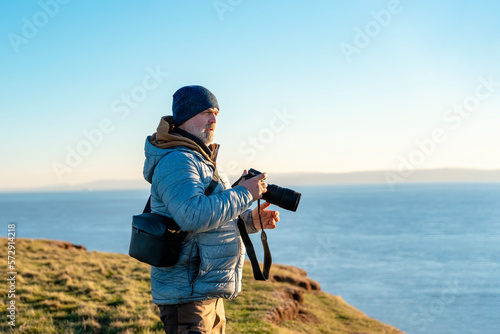 Bearded Man reaching the destination at sunset on cool day and taking photos of amazing seaside landscape in Wales. Travel Lifestyle concept.