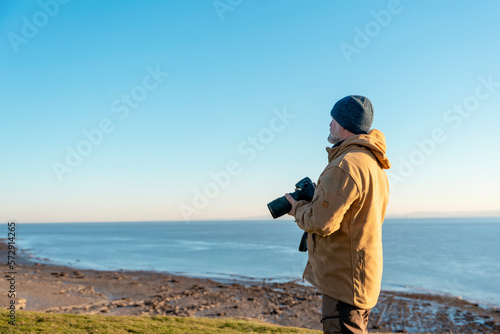 Bearded Man reaching the destination at sunset on cool day and taking photos of amazing seaside landscape in Wales. Travel Lifestyle concept.